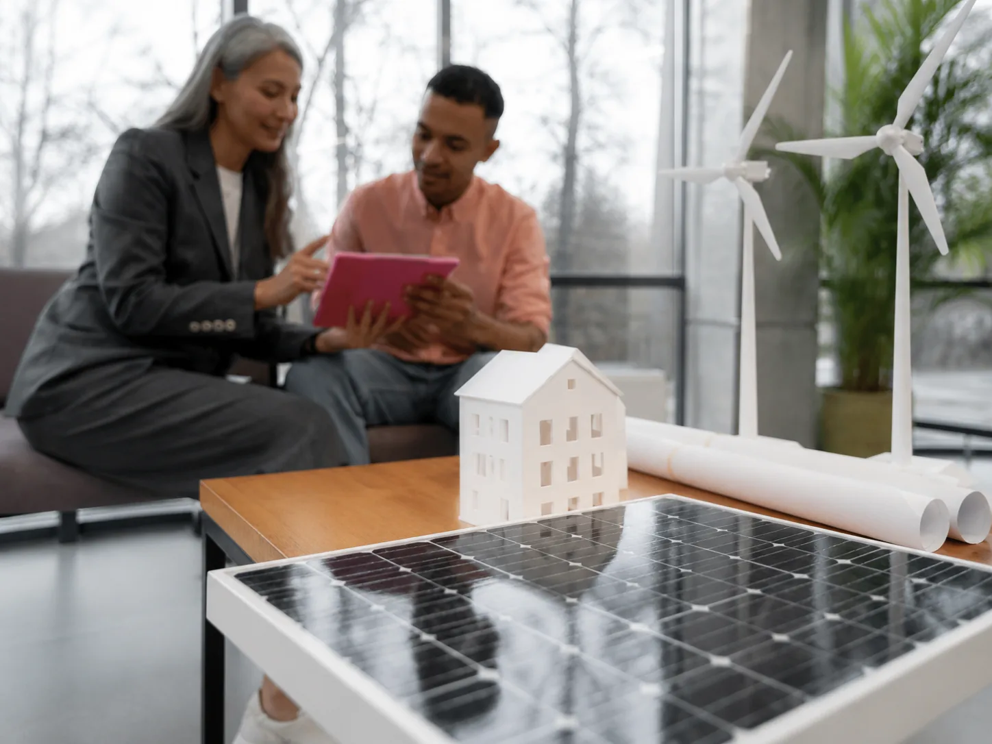 Consultants discussing renewable energy planning with solar model and wind turbines